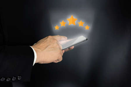 close up on customer man hand pressing on smartphone screen with gold five star rating feedback icon and press level excellent rank for giving best score point to review the service , business conceptの写真素材