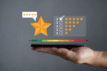 close up on customer man hand pressing on smartphone screen with gold five star rating feedback icon and press level excellent rank for giving best score point to review the service , business conceptの写真素材