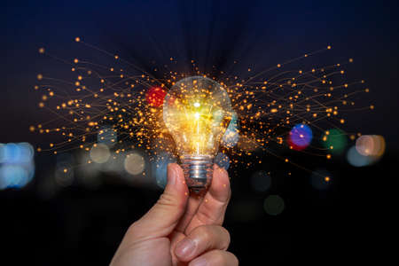 Hand holding light bulb glowing with orange light line and ray. Creative and new business idea concept.の写真素材