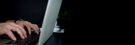 A man using laptop computer working on new project idea at his desk in the office late at night, panoramic web banner with copy space on the rightの写真素材