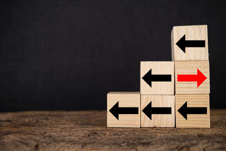 Wood block red arrow pointing the opposite way disruptive from the black arrows on table wooden....