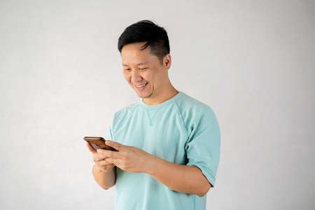 Attractive man with short dark hair chatting or typing text message using cell phone isolated over white backgroundの写真素材