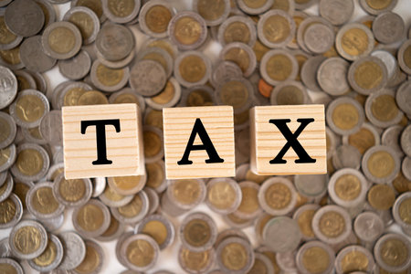 Tax Concept with wooden block on stacked coins. Wooden cubes with the word Tax on money pile of coinsの写真素材