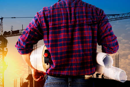 Double exposure image of construction worker holding safety helmet and construction drawing against the background of surreal construction site in the city.の写真素材
