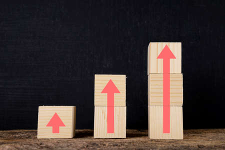Wooden blocks stacked in steps with red arrows on the table, black background. Business growth success process concept. copy spaceの写真素材