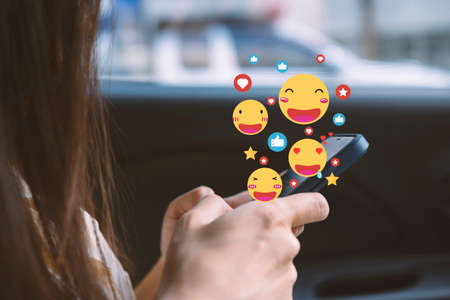 Close-up of a woman in a soft shirt using the smart phone, hands holding and typing to communicate with others through emoji and text online.の写真素材