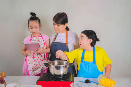 The mother and daughter were standing in the kitchen next to a wooden table about to put butter in the pot and were looking for information on tablets.の写真素材