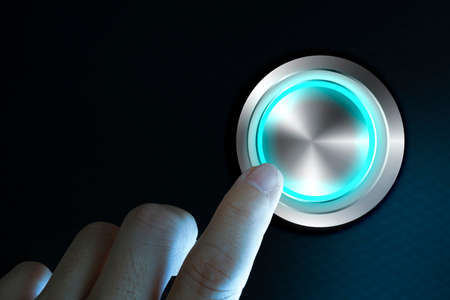 Finger about to press button with blue light over black and grey background. Concept image for illustration of change or strategic vision.の写真素材