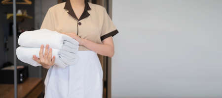 Young chambermaid putting stack of fresh towels in bedroom, Space for textの写真素材