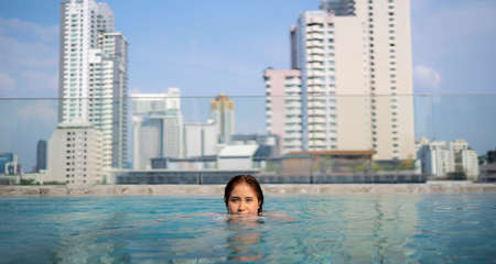 Young woman in the swimming pool. The swimming pool on the rooftop is a large building in the background.の写真素材