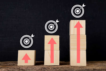 Wooden blocks stacked in steps with red arrows on the table. Chalkboard background with arrows...