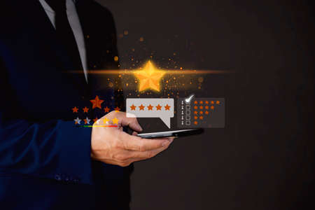 Close up on customer man hand pressing on smartphone screen with gold five star rating feedback icon and press level excellent rank for giving best score point to review the service , business conceptの写真素材