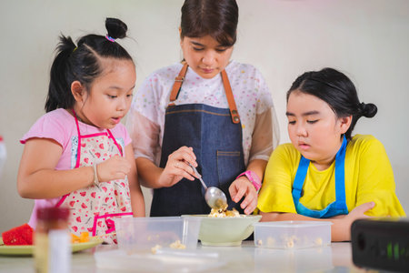 Asian mother and daughter enjoy making popcorn, Asian mom teaching daughter to learn making popcorn in real life kitchen at homeの写真素材