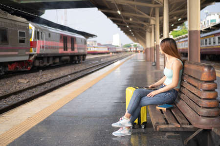 woman traveler waiting fot the train, sitting and using smartphone at train stationの写真素材