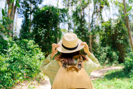 Asian woman traveler with backpack holding hat and looking at amazing mountains and forest, travel...