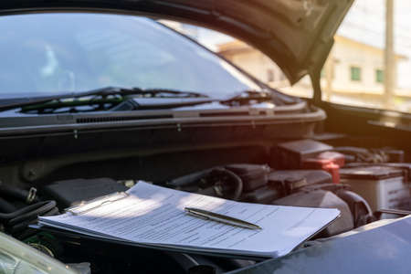 Clipboard on car with car insurance claim form for customer maintenance vehicle checklist in auto repair shop garage. Engine repair service concept. Business technical mechanics support for fixing carの写真素材
