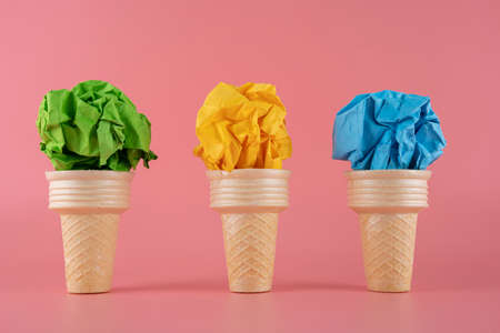 Green, yellow, blue paper cubes placed inside an ice cream cone on a pink background.の写真素材