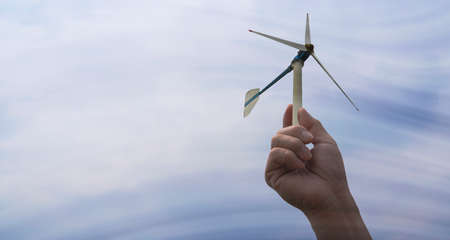 Hand holding a sustainable green energy wind turbine. The wind is moving through the turbines.の写真素材