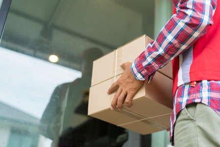 A man delivering parcels is standing at the door of the house waiting for customers to pick them up in a polite manner.の写真素材