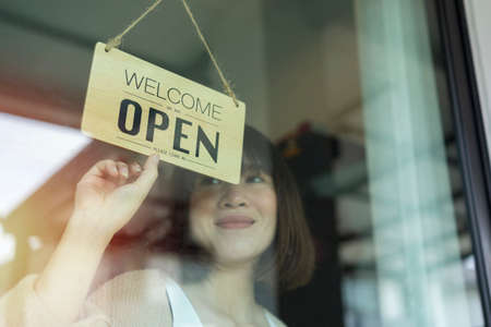 Asian young asian woman setting open sign at the shop glasses for welcome the customer in to the coffee shop, small business owner and startup with cafe shop, installing open and close label conceptの写真素材