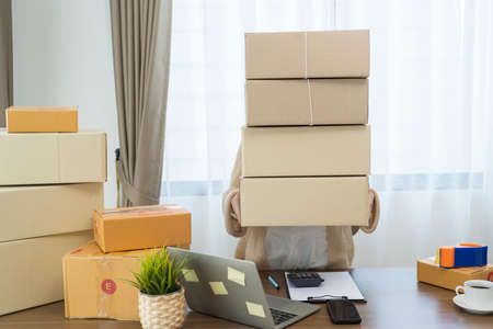 Asian woman holding parcel boxes and checking orders from laptop, she owns an online store, she packs and ships through a private transport company. Online selling and online shopping concepts.の写真素材