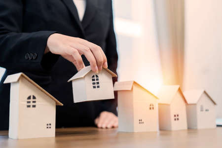 Business woman choosing mini wood house model from model on wood table, Planning to buy property. concept of Choose the best.の写真素材