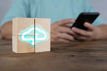 Concept of cloud computing. Stack of wooden block cube with computing icon online connection database digital. Background is a man using a smartphone.の写真素材