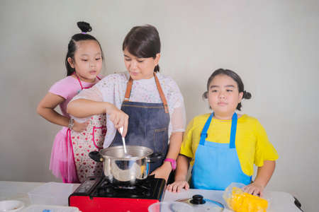 happy family in kitchen. young asian mother and child daughter preparing dough bake cookies for birthday. adorable kid with mom mix flour and egg together in bowl at home. elegant woman look at girlの写真素材