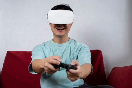 Excited and shocked face of Asian gamer with headphone holding joystick playing video game online sitting on chair at living room. professional gamer streaming on social playing game very funの写真素材