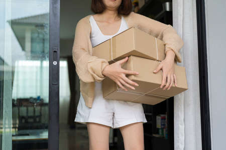 Indoor image of happy cheerful young woman holding cardboard box delivered to her, expressing excitementの写真素材