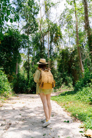 Woman traveling in forest nature with backpack and straw hat. Traveler woman with backpack walking on path in jungle tropical forest, Tourism beautiful destination resort. Vertical shot.の写真素材