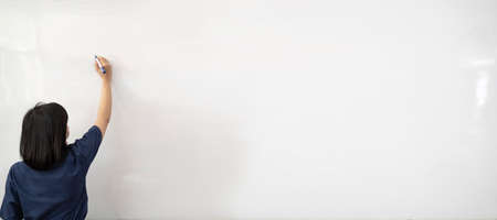 Woman in white shirt writing on imaginary screen whiteboard with blue marker on white background. Back view. Half length portrait. Teacher, office worker.の写真素材