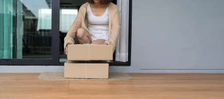 Deliver parcels box on door mat near home entrance door. Woman receiving parcel at the door, Delivery online order to home. Panoramic images for use with bannersの写真素材