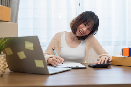 Young business woman working online e-commerce shopping at her shop. Young woman seller prepare parcel box of product for deliver to customer. Online selling, e-commerce.の写真素材