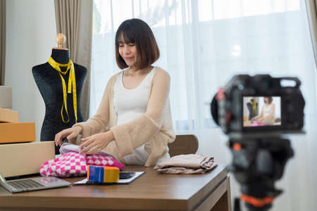 Young Asian woman entrepreneur talking camera live recording video on social network at home. Online selling, work at home, business and technology conceptの写真素材