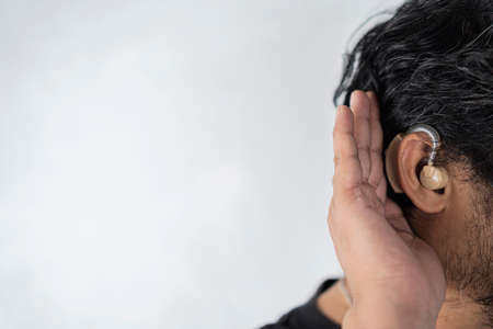 Close-up Of A Man's Hand Inserting Hearing Aid In His Ear. A man in his late 40s began to have difficulty hearing and had to use a hearing aid.の写真素材