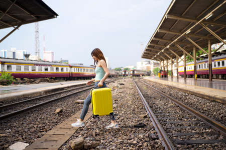 An elegant woman with a suitcase traveling by rail autumn day. Travel across the railroad to get on the train.の写真素材