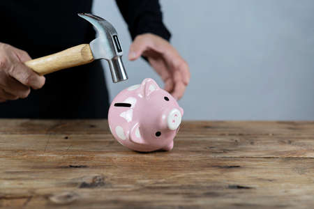 Hand with hammer about to smash piggy bank to get at savingsの写真素材