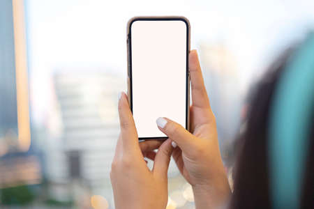 Back view of crop female with short hair wearing white shirt and eyeglasses taking picture on mobile phone while standing in street on sunny dayの写真素材