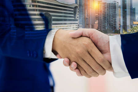Close up of handshake on abstract city background. Teamwork concept. Double exposure. Filtered imageの写真素材