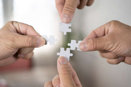 Closeup image of many people holding and putting a piece of white jigsaw puzzle togetherの写真素材