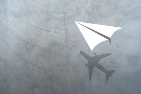 Paper plane in mid flight with shadow of a real plane. Cement texture surface of wall loft style background.の写真素材