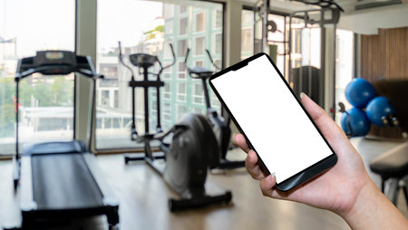Hand holding smartphone device at gym background. interior of modern fitness center gym with equipmentの写真素材