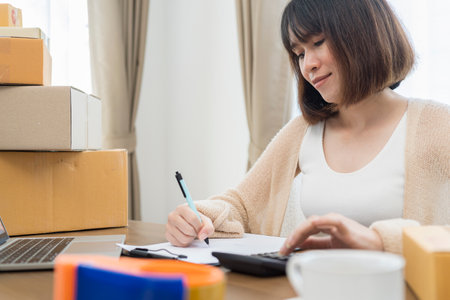 Online seller Close up hands Young asian woman typing laptop keyboard checking online order, check goods stock delivery package shipping postal. Asian woman startup small business at home officeの写真素材