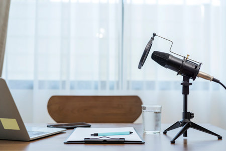 Studio microphone for recording podcasts sits on a table with a laptop, recording paper, pen and a glass of water. in the office at homeの写真素材
