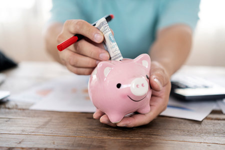 A businessman puts a dollar in a small piggy bank thinking about investing savings.の写真素材