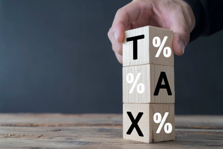 Tax deduction planning concept. Expenses, account, VAT, income tax, and property tax, businessman hand holding tax icon on wooden blockの写真素材