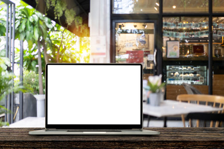 Blank screen laptop computer on wood table top with blur cafe restaurant with abstract bokeh light defocused backgroundの写真素材