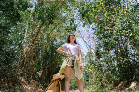 A young female climber stands in the lush forest and looks at the trees. standing in the middle of the green forestの写真素材