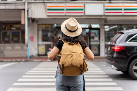 Girl carrying a backpack with a straw hat crossing the road . Traffic rules in Bangkok, Thailand.の写真素材